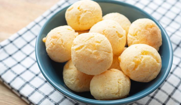 Imagem de um bowl azul sobre um pano xadrez com pães de queijo.