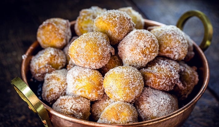 Em cima de uma mesa, balde de metal com bolinhos de chuva, polvilhado com açúcar de confeiteiro.