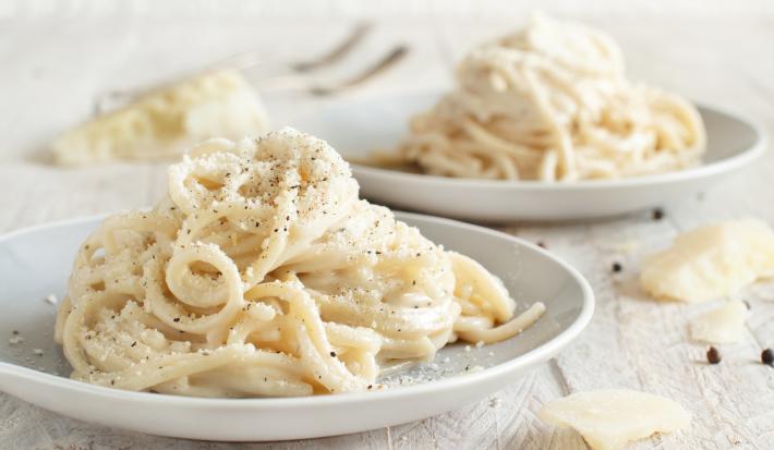 Foto da receita de Macarrão Cacio e Pepe. Observa-se dois pratos com o macarrão espaguete, polvilhado de queijo e pimenta-do-reino preta.