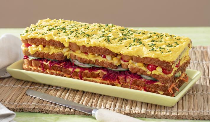 Foto da receita de Torta Fria Vegetariana. Observa-se a torta em um recipiente retangular com camadas de legumes e maionese. No topo, maionese com cheiro-verde bem picadinho.