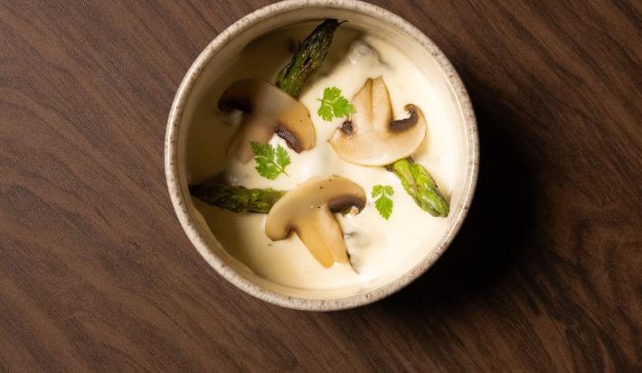 Foto da Receita de Escargot com Creme de Batatas e Natas. Observa-se uma tigela vista de cima com o creme de batatas e decorada com cogumelos, cabeças de aspargos e ramos de salsinha (cerefólio)