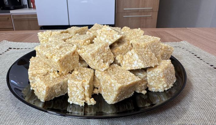 Fotografia em tons claros com vários quadradinhos feitos com amendoim, leite moça e tostines maisena ao centro. Os quadradinhos possuem cores caramelizadas e crocantes de amendoim e tostines