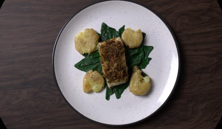 Fotografia em tons de branco com um prato branco ao centro. Dentro do prato existe uma receita de bacalhau acompanhado de batatas amassadas e espinafre.