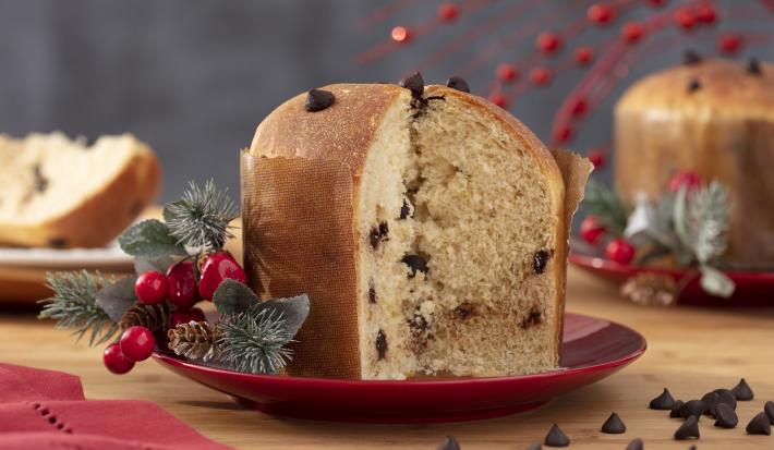 Imagem de um panetone caseiro com gotas de chocolate cortado em um prato vermelho, com decorações de Natal.