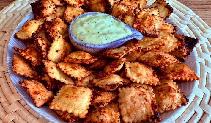 Fotografia mostra raviolis dourados sobre um prato branco. Ao centro, um molho verde.