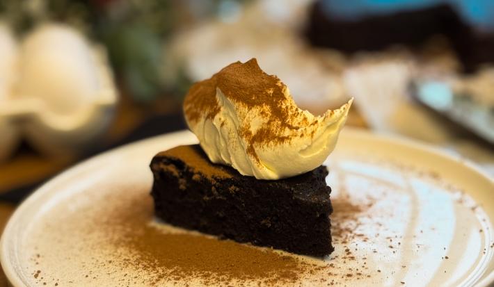 Fotografia de uma fatia do fondant em um prato grande branco raso branco. Por cima tem um creme e chocolate em pó polvilhado.