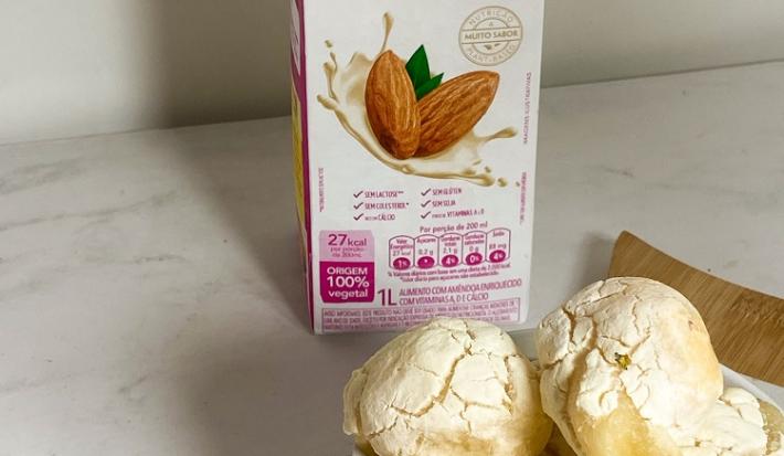 Foto da receita de pão de queijo vegano servida em diversas porções em um prato de porcelana branca sobre uma tábua de madeira com uma embalagem de nature's heart bebida de amêndoa ao fundo