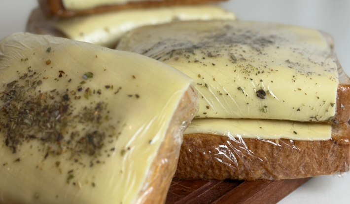Fotografia mostra sanduíches embalados em plástico filme. As fatias de pão de forma aparecem cobertas por queijo com orégano polvilhado