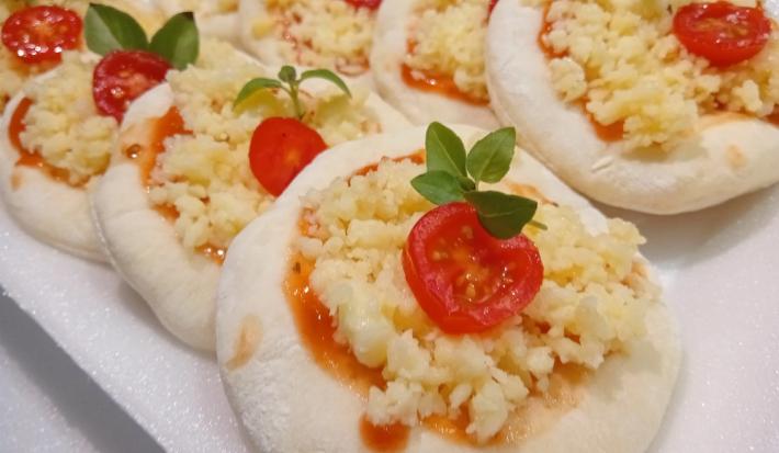 Foto da receita de Mini Pizza. Observa-se os discos pequenos um ao lado do outro, recheados com molho de tomate, queijo, tomate cereja e manjericão.