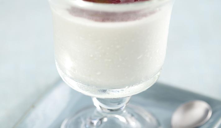 Fotografia em tons de cinza em uma mesa de madeira cinza com um prato quadrado azul claro e uma taça de vidro em cima com o mousse de iogurte com geleia de frutas vermelhas.