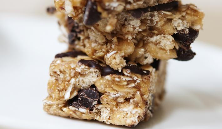 Fotografia de barrinhas de cereal de mel com aveia cobertas por chocolate. As barrinhas estão uma sobre a outra.