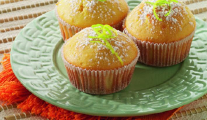Fotografia em tons de verde, branco e amarelo, ao centro prato verde sobre guardanapo laranja, com três bolinhos decorados com raspas de laranja e açúcar, tudo sobre toalha branca alinhavada.