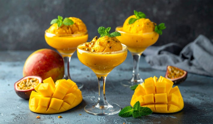 Fotografia em tons claros com alguns potes de sorvete ao centro. Dentro de cada pote existe um sorvete de manga com maracujá super refrescante para o calor