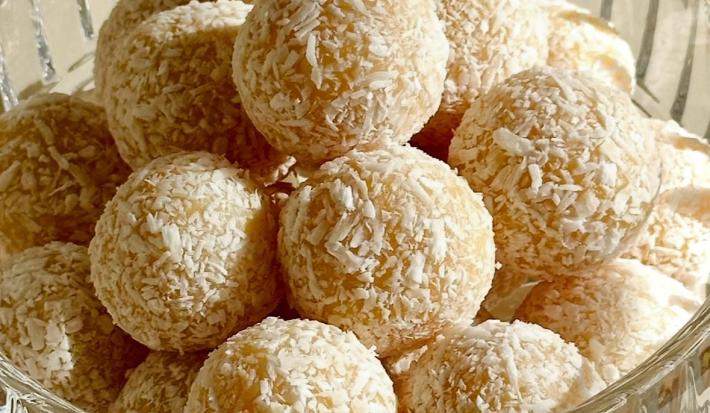 Fotografia em tons de branco com um pote de vidro ao centro. Dentro do pote existe várias unidades de brigadeiro de chocolate branco finalizados com coco ralado