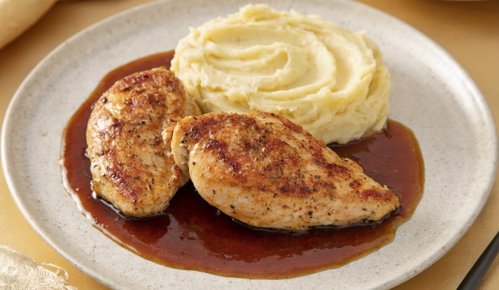 Pedaços de frango dourados servidos com purê cremoso de batata e molho escuro reduzido, apresentados em prato branco elegante