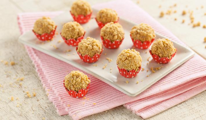 Fotografia em tons de branco e vermelho de bancada de madeira branca, pano rosa dobrado, um brigadeiro de paçoca sobre o pano, prato retangular branco com nove brigadeiros de paçoca em forminhas vermelhas com bolinhas brancas. Fotografia em tons de branco e vermelho de bancada de madeira branca, pano rosa dobrado, um brigadeiro de paçoca sobre o pano, prato retangular branco com nove brigadeiros de paçoca em forminhas vermelhas com bolinhas brancas.