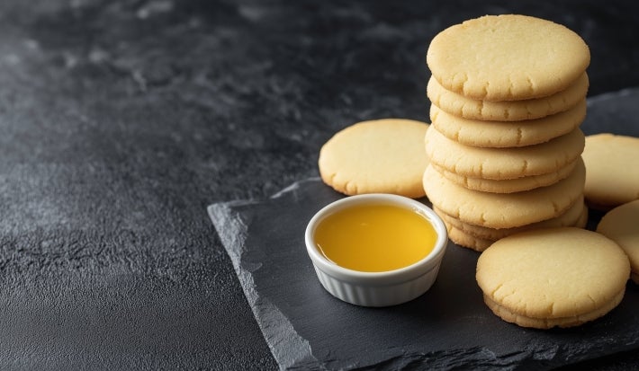 Em cima de uma mesa, biscoitos amanteigados dourados e redondos crocantes.