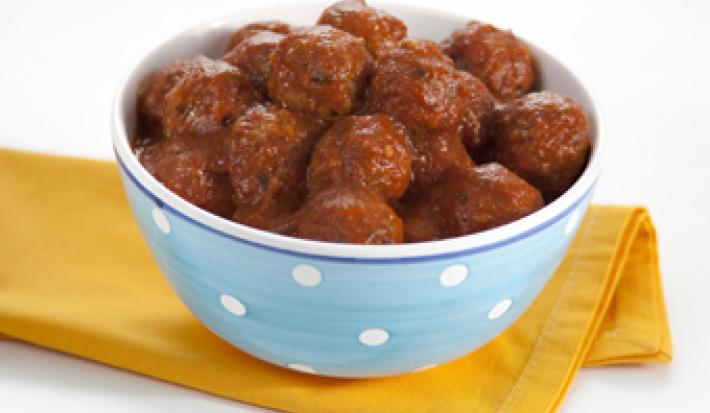 fotografia em tons de amarelo e branco, contém um pano amarelo e por cima um recipiente redondo azul com bolinhas brancas que contém bolinhos de carne com molho de tomate por cima