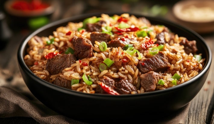 Em um cima de uma mesa, tigela redondo com arroz, carne de boi picada e pimentão, decorado com cebolinha picada.