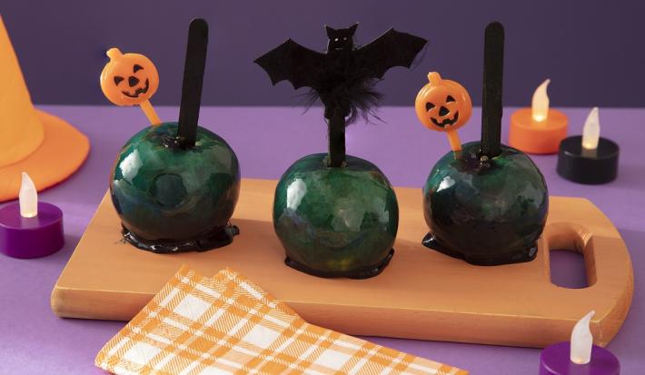 Foto da receita de maçã do amor da bruxa malvada servida em 3 porções sobre uma tábua de madeira com decoração de halloween em volta