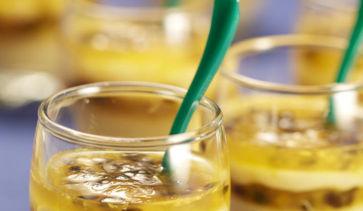 fotografia em tons de azul e amarelo, contém diversas taças com o doce de maracujá feito com camadas de creme e polpa de maracujá.