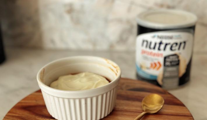 Foto da receita de cookie de airfryer feito com Nutren Protein, servido e um pote branco com uma cobertura branca por cima e a lata do produto ao fundo