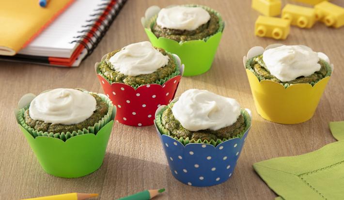 Fotografia de cinco muffins de espinafre, cada um dentro de forminhas coloridas. Sobre cada um tem um creme caseiro com ninho, e estão sobre uma mesa de madeira.