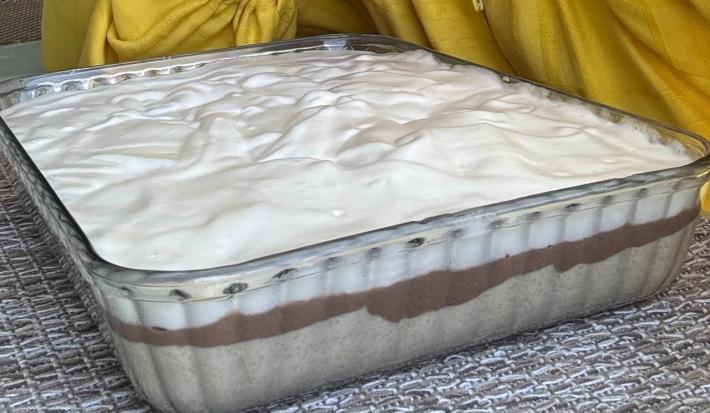 Fotografia em tons de amarelo em uma bancada de madeira com uma travessa de vidro e a torta de farinha láctea nestlé dentro.