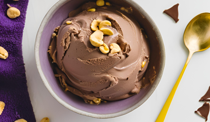 Fotografia em tons de branco com uma tigela ao centro. Dentro da tigela existe um sorvete de chocolate com pedaços de amendoim em cima.