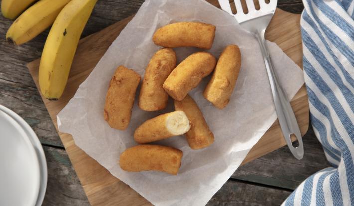 Imagem vista de cima de bananas a milanesa em cima de uma tábua de madeira