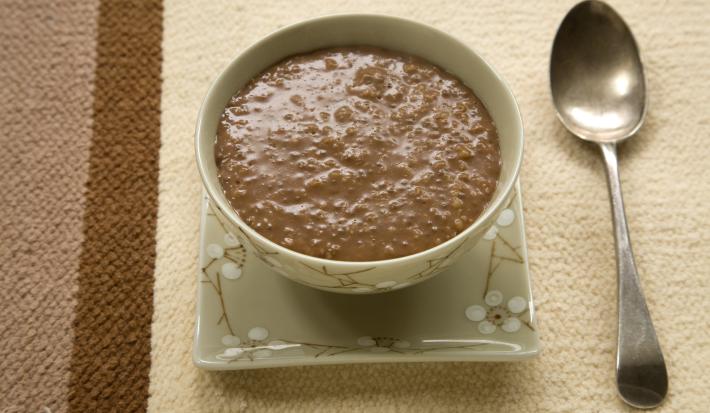 Fotografia de um mingau de chocolate servido em uma tigela, em tons verdes e estampa de flores branca.