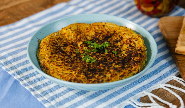 Fotografia em tons de azul com um prato azul ao centro. Em cima do prato existe uma receita de batata-doce rosti recheada com carne desfiada
