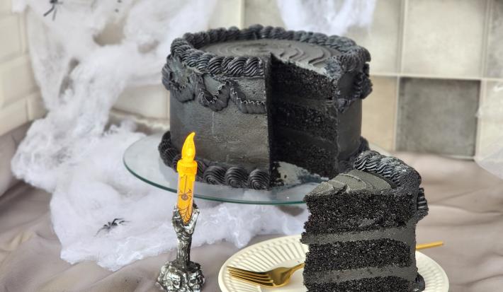 Foto da receita de Bolo de Veludo Preto. Observa-se um bolo alto preto decorado de preto, com uma decoração de Dia das Bruxas.