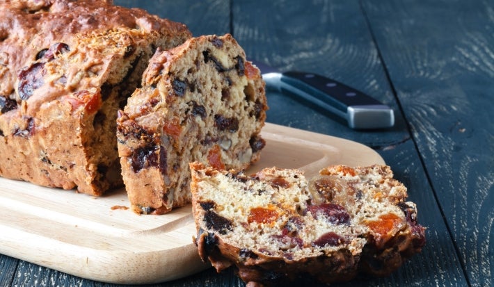A imagem mostra um bolo de frutas secas e castanhas já fatiado, sobre uma tábua de madeira. É um bolo rústico, com aparência caseira e textura densa, repleto de pedaços visíveis de frutas como damasco, uvas-passas, figos e nozes. A imagem mostra um bolo de frutas secas e castanhas já fatiado, sobre uma tábua de madeira. É um bolo rústico, com aparência caseira e textura densa, repleto de pedaços visíveis de frutas como damasco, uvas-passas, figos e nozes.