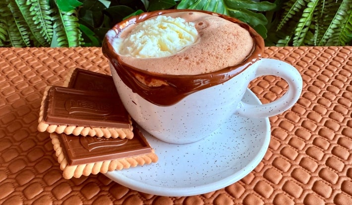 Fotografia em tons terrosos com uma xícara branca ao centro. Dentro da xícara existe uma receita de Affogato café feita com uma cápsula Kopenhagen, acompanhada de Nestlé Chocobiscuit
