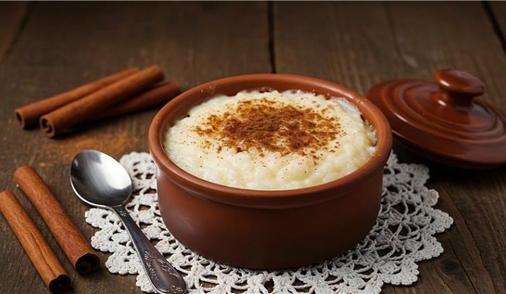 Em cima de uma mesa, tigela com arroz doce cremoso, com uma textura suave e aveludada, decorado com canela em pó.