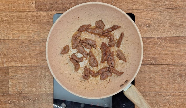 Tiras de carne bovinas douradas sobre frigideira de fundo claro