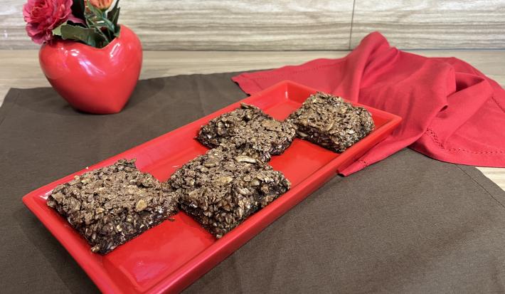 Fotografia em tons de marrom e vermelho com uma régua vermelha ao centro. Em cima deste prato existe 4 barrinhas de cereal em formato quadrado feita com NESTLÉ Aveia Flocos e NESCAU Extra Cacau 30%