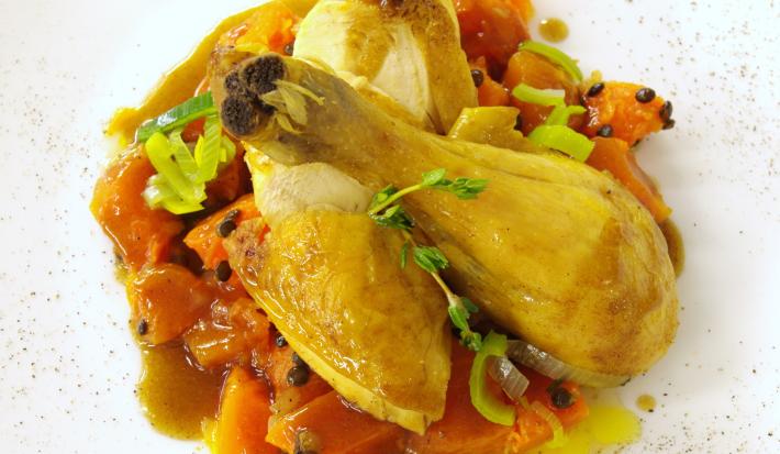 Fotografia vista de cima de um frango ensopado com abóbora e leite de coco sobre um prato branco com pimenta preta salpicada por cima.
