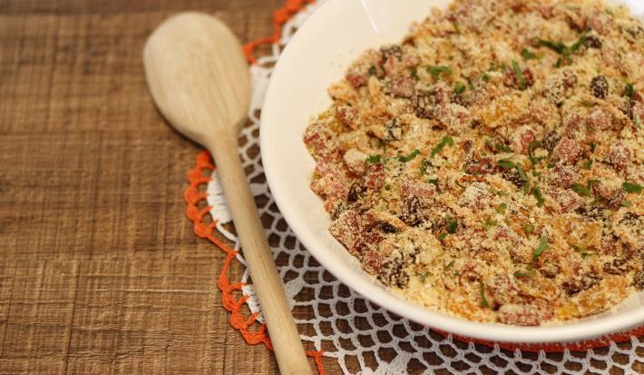 Foto da Receita de Farofa Rica Natalina, fácil e deliciosa, feita com bacon, calabresa, linguiça toscana e farinha de mandioca torrada, servida sobre uma mesa de madeira, com uma colher de pau ao lado