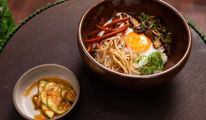 Bibimbap vegetariano com arroz japonês, legumes coloridos salteados e ovo de gema mole, acompanhado de molho picante