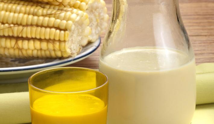 foto tirada de uma jarra com suco de milho e à frente um copo amarelo com a bebida