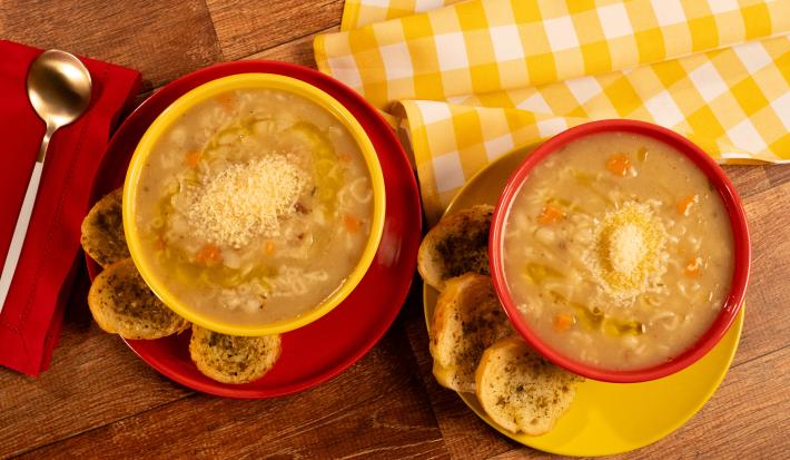 Fotografia mostra duas cumbucas com sopa de carne com legumes e queijo povilhado sobre um prato. Ao lado, torradas temperadas.