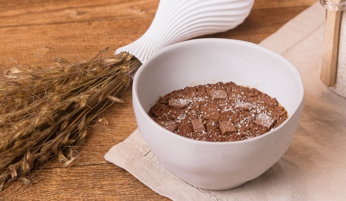 Receita de massa de brownie comestível servida em um pote branco sobre uma mesa de madeira decorada com alecrim