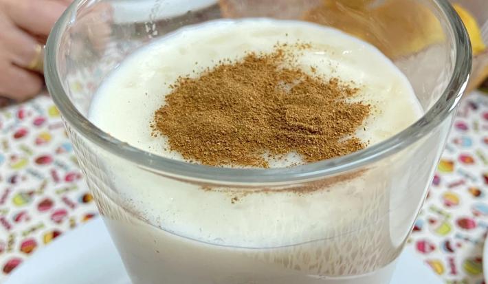 Foto aproximada da receita de Arroz Doce, servido em um taça polvilhado com canela, sobre uma mesa com uma toalha estampada e colorida