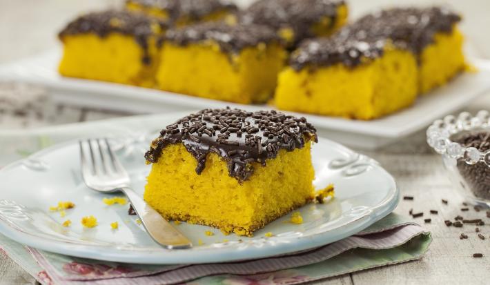 Foto de um pedaço de bolo de cenoura com cobertura de brigadeiro em um prato branco com um garfo do lado