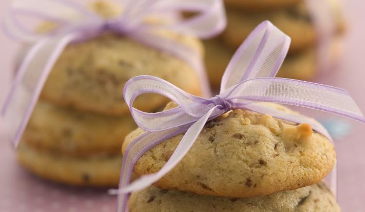 Foto com 3 cookies um em cima do outro amarrados com um cetim rosa, no fundo da foto há outros 2 cookies da mesma maneira