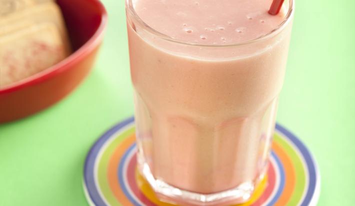 fotografia em tons de verde e rosa tirada de um copo transparente com a vitamina de frutas, e por cima um coração para decorar