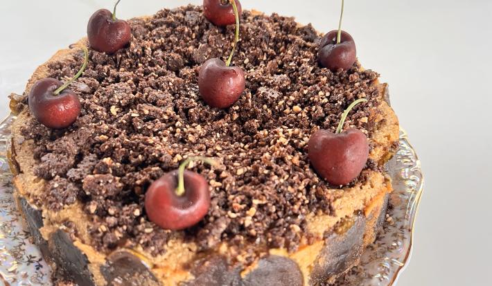 Fotografia em tons de branco com um bolo de Cuca de maçã verde ao centro enfeitada com cerejas