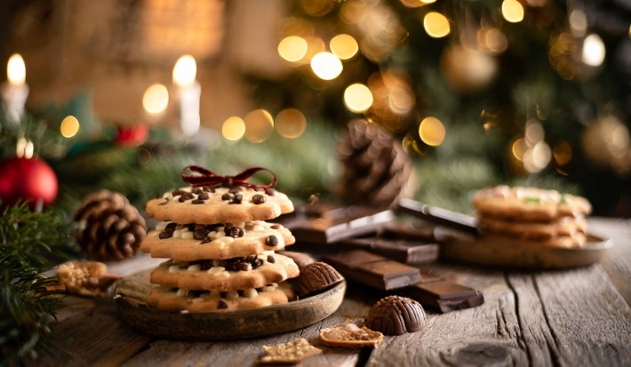 Em cima de uma mesa, em cima de um prato, biscoitos com gotas de chocolate perfilado um em cima de outro, decorado com um laço marrom.